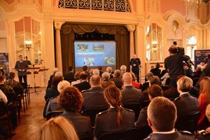 widok ogólny na salę lustrzaną pałacu, w którym odbywa się konferencja. Komendant stoi za mównicą i rozpoczyna konferencję.