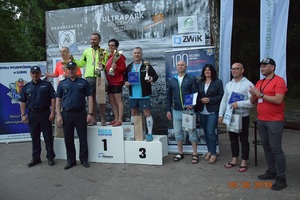 Wszyscy finaliści biegu w sportowych strojach obok podium oraz komendanci w mundurach.