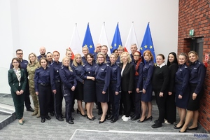 Grupa osób w Sali konferencyjnej uczestniczących w spotkaniu - kobiet i mężczyzn, policjantów i pracowników Policji. W tle flagi Polski i Unii Europejskiej.