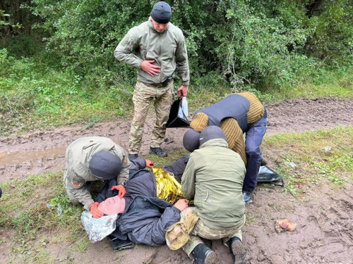 Trzej mężczyźni udzielają pomocy leżącemu na ziemi rannemu mężczyźnie, czwarty funkcjonariusz stoi przy nich i trzyma w ręku torbę.