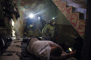 Policjanci w umundurowaniu taktycznym podchodzą do mężczyzn leżących na podłodze.