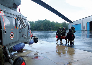 Policjanci wynoszą na noszach z helikoptera rannego.