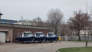 Trzy policyjne łodzie na przyczepach do transportu na podjeździe do budynku.