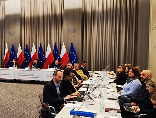 Sala konferencyjna, za stołem prezydialnym stoją flagi Polski i UE.