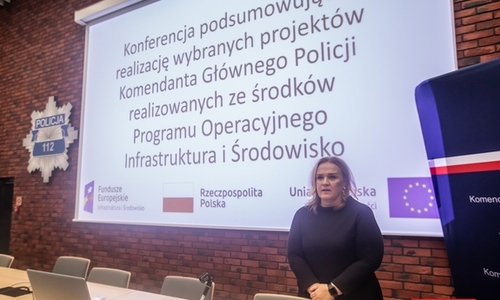 kobieta stojąca na tle ekranu, na którym wyświetlany jest napis Konferencja podsumowująca realizację projektów Komendanta Głównego Policji realizowanych ze środków Programu Operacyjnego Infrastruktura i Środowisko.