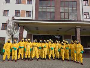 Zdjęcie przedstawia uczestników szkolenia w żółtych kombinezonach ochronnych, którzy pozują na tle budynku, w którym odbywa się szkolenie.