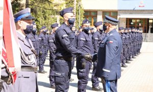 Umundurowani policjanci stojący w szeregu. Na pierwszym planie dwaj policjanci podają sobie dłonie