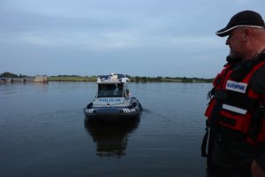 Ratownik stojący na pomoście, patrzy na policyjną łódź na wodzie