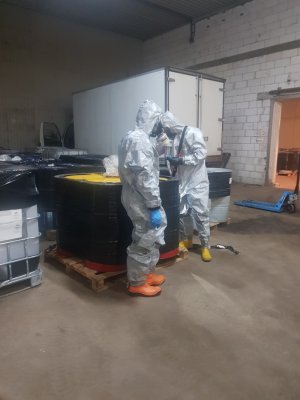 Funkcjonariusze w specjalnych kombinezonach przy zabezpieczonych pojemnikach z chemikaliami