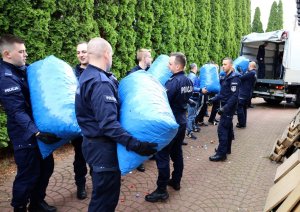 Policjanci pakujący na ciężarówkę worki z zakrętkami