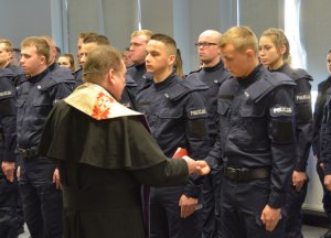 Ksiądz oraz umundurowani policjanci stojący w szeregu