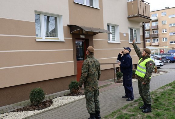 Policjanci i żołnierze stojący przed blokiem