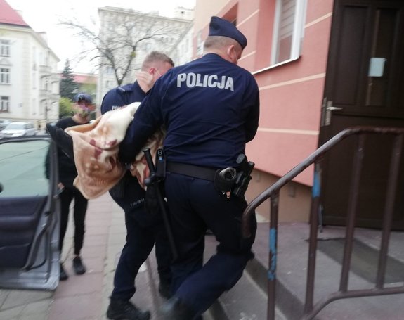 Umundurowani policjanci niosący starszą osobę