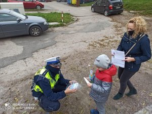 Policjant sochaczewskiej drogówki przekazuje maseczkę ochronna dziecku i jego mamie