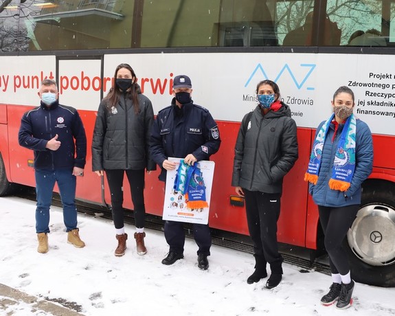 Policjanci oraz siatkarki stojące obok autobusu