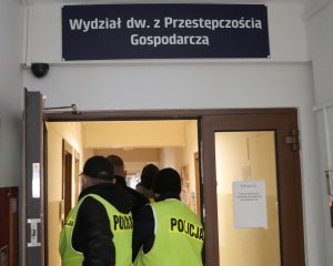 Policjanci ubrani w kamizelki odblaskowe prowadzą zatrzymanego mężczyznę