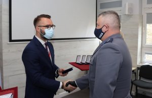 Umundurowany policjant oraz cywil stojący w maseczkach