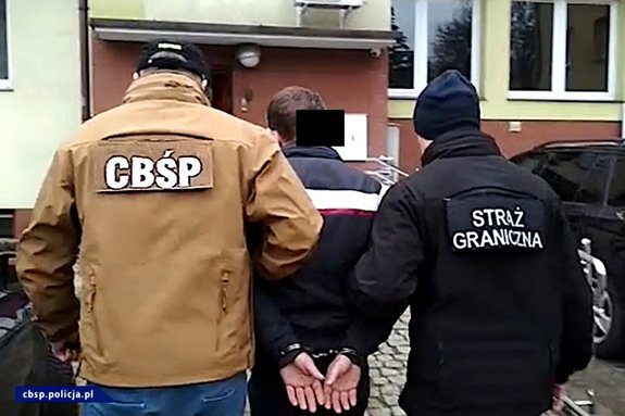 Policjant CBŚP, funkcjonariusz SG prowadzą osobę zatrzymaną