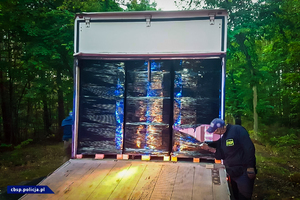 policjant CBŚP przeszukuje pojazd ciężarowy, na pojeździe ofoliowane palety z kartonami