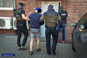 Policjanci CBŚP i funkcjonariusz KAS prowadzą osobę zatrzymaną