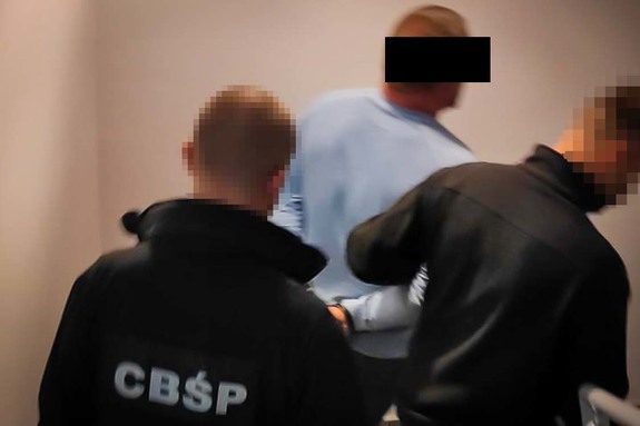 Dwóch policjantów w ubiorach cywilnych, prowadzi zatrzymanego po schodach.