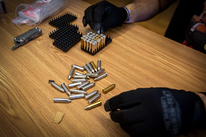 Policjant wkladający do plastikowych koszyczków amunicję leżącą na blacie stołu.