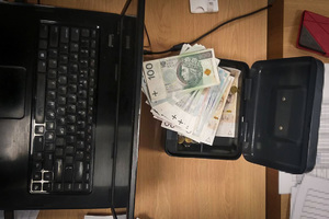 Banknoty o różnych nominałach leżące w metalowej kasetce. Obok laptop.