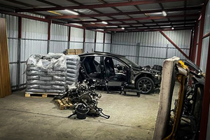 Częściowo rozebrany samochód oraz palety z workami stojące w blaszanym garażu