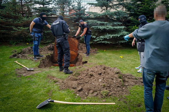 Funkcjonariusze niemieckiej policji odkopujący skrytkę ziemną umieszczoną pod trawnikiem.