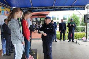 Policjant wręcza dyplomy stojącym na podium uczestnikom turnieju