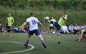 Fotografia kolorowa przedstawiająca boisko na którym zawodnicy rozgrywają mecz. W tel widoczni kibice.