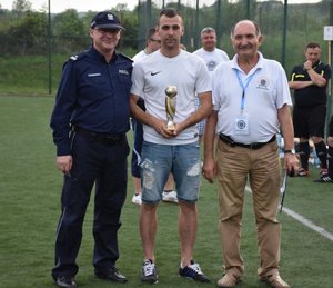 Fotografia kolorowa na której od lewej strony widać Komendanta Powiatowego Policji w Łańcucie, w dalszej kolejności zawodnika z pucharem w rękach oraz przedstawiciela IPA.