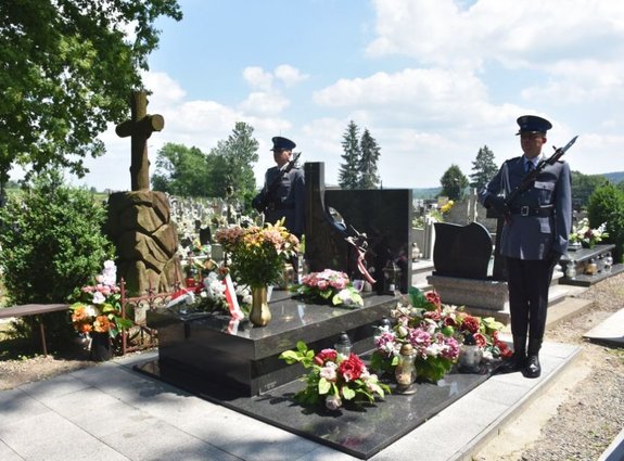 Zdjęcie kolorowe wykonane na cmentarzu. Na fotografii widać nagrobek gen. Marka Papały. Przy nagrobku znajduje się dwóch policjantów z ostrą bronią, którzy pełnią wartę honorową