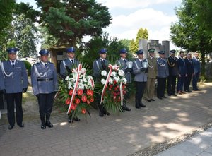 Fotografia kolorowa przedstawiająca umundurowanych policjantów którzy trzymają dwa wieńce.