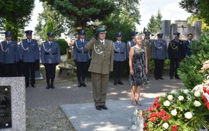 Fotografia kolorowa na której widać funkcjonariusza SG oddającego hołd zmarłemu. Obok mężczyzny po prawej stronie stoi kobieta.