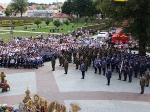 Kolorowa fotografia. Widok z balkonu bramy wejściowej do Bazyliki. Na dole kompanie reprezentacyjne służb mundurowych ustawione w szyku, rolnicy, zaproszeni goście i wierni.