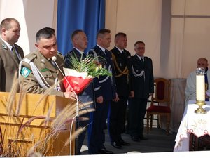 Kolorowa fotografia. Najwyższy rangą przedstawiciele służb mundurowych stoją w rzędzie na ołtarzu polowym. Generał Straży Granicznej z ambony wygłasza podziękowanie dla księdza biskupa.