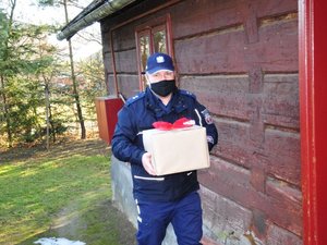 fotografia przedstawia Zastępcę Komendanta Powiatowego Policji w Jaśle w umundurowaniu służbowym, niosącego prezent przygotowany w ramach akcji Szlachetna Paczka