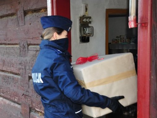 fotografia przedstawia policjantkę w umundurowaniu służbowym, niosącą przygotowany prezent w ramach akcji Szlachetna Paczka