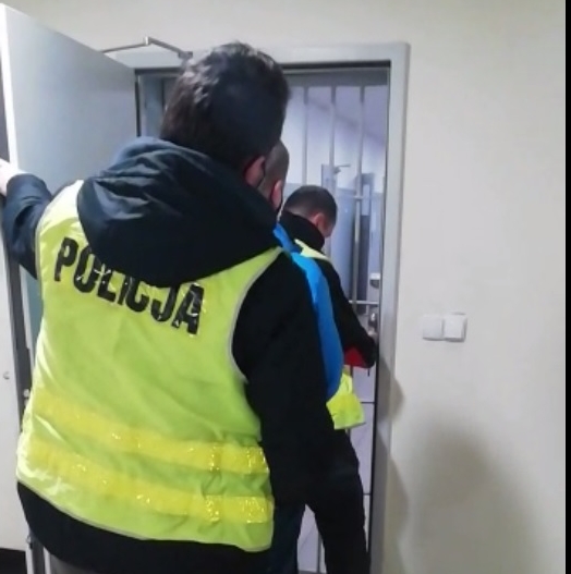 policjant w kamizelce z napisem policja prowadzi podejrzanego