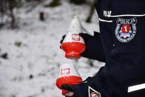 Złożenie kwiatów i zapalenie zniczy przy obelisku upamiętniającym katastrofę śmigłowca w Cisnej przez policjantów. Zbliżenie na dwa biało-czerwone znicze w rękach policjanta.