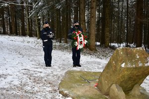 Złożenie kwiatów i zapalenie zniczy przy obelisku upamiętniającym katastrofę śmigłowca w Cisnej przez policjantów. Policjantka i policjant stoją przed obeliskiem z wieńcem i zniczami.