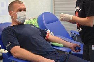 Policjant siedzący na fotelu w krowiobusie w trakcie oddawania krwi.