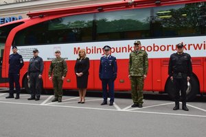 Przedstawiciele służb mundurowych stoją przed krwiobusem. W środku Ewa Zawilińska Dyrektor RCKiK w Rzeszowie oraz Komendant Wojewódzki Policji w Rzeszowie insp. Dariusz Matusiak.