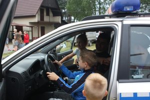 na fotografii policjant w radiowozie wraz z dziećmi, pokazuje uczestnikom spotkania radiowóz