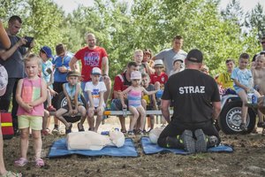 na fotografii strażak z grupą dzieci, uczy jak udzielać pierwszej pomocy