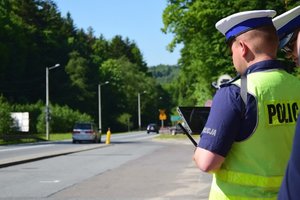 Dwaj policjanci ruchu drogowego, umundurowani i w odblaskowych kamizelkach, trzymają w rękach panel sterowania dronem.