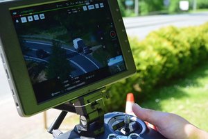 Dwaj policjanci ruchu drogowego, umundurowani i w odblaskowych kamizelkach, trzymają w rękach panel sterowania dronem.