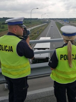 Policjantka i policjant w kamizelkach podczas działań mierzą odległości między jadącymi pojazdami za pomocą specjalnego urządzenia.