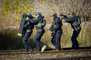 Policyjni antyterroryści idą w szeregu wzdłuż torowiska. Pierwszy z lewej trzyma tarczę ochronną